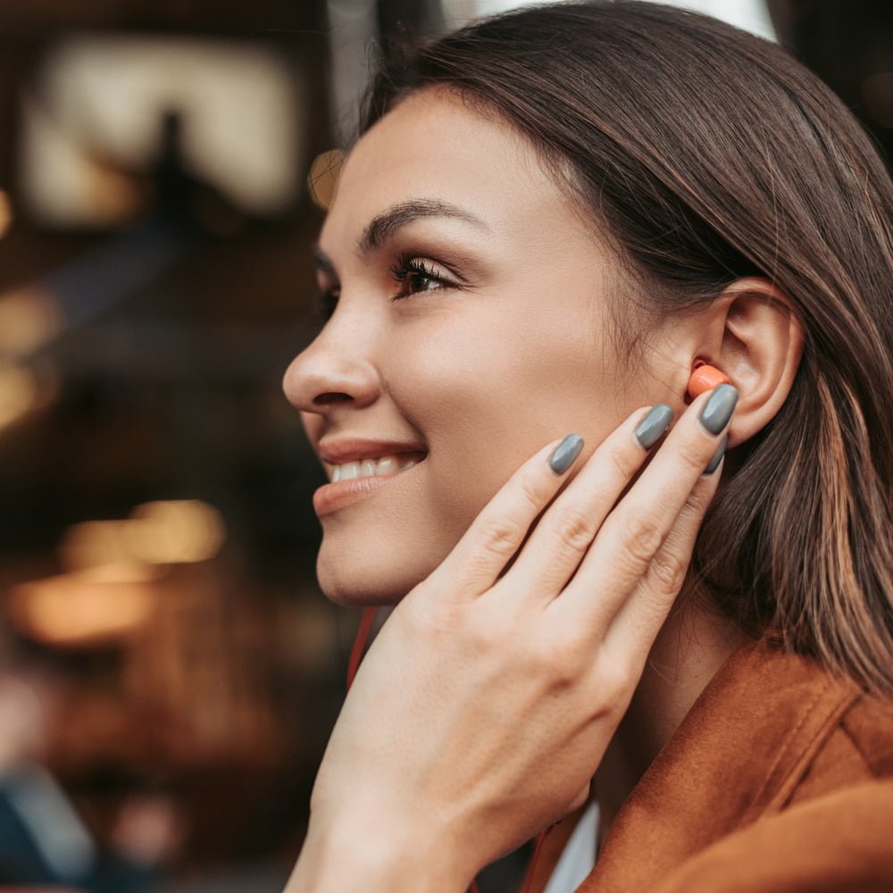 Smiling woman with brown hair wearing earplugs as hearing protection.