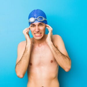 Young swimmer man covering ears with hands, assuming he has effects of swimmer's ear