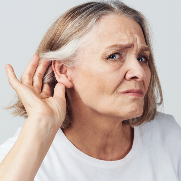 Senior woman looking at camera, holding her hand to her ear on hearing loss journey.