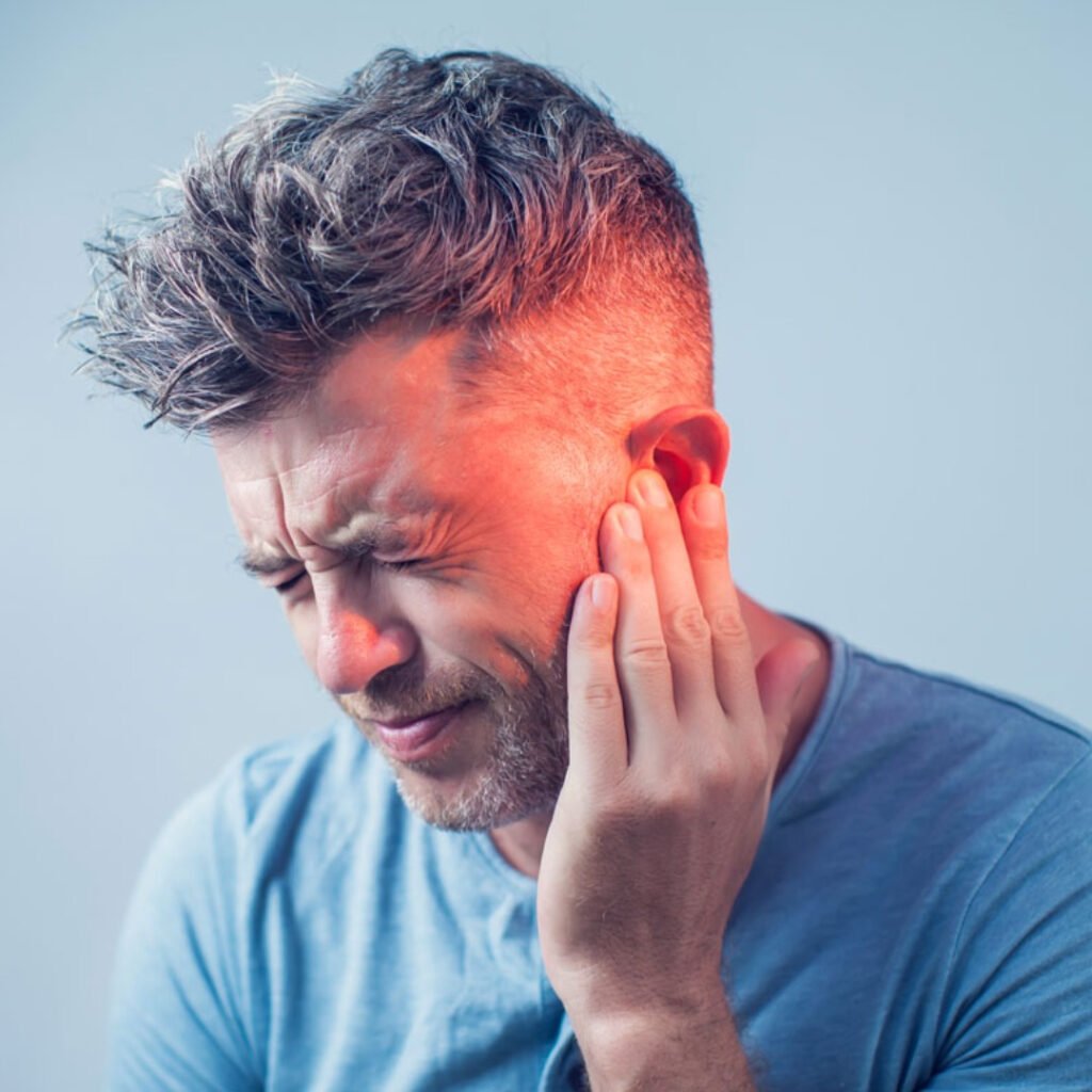 Middle-aged man grimacing, holding hand up to ear, suffering from ear pain due to hearing loss and tinnitus.